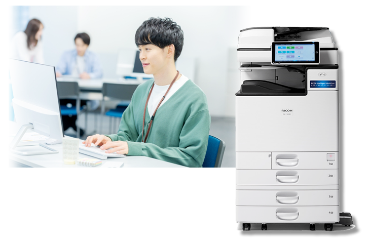 RICOH リコーカラー複合機とオフィスでパソコンを使う人の写真